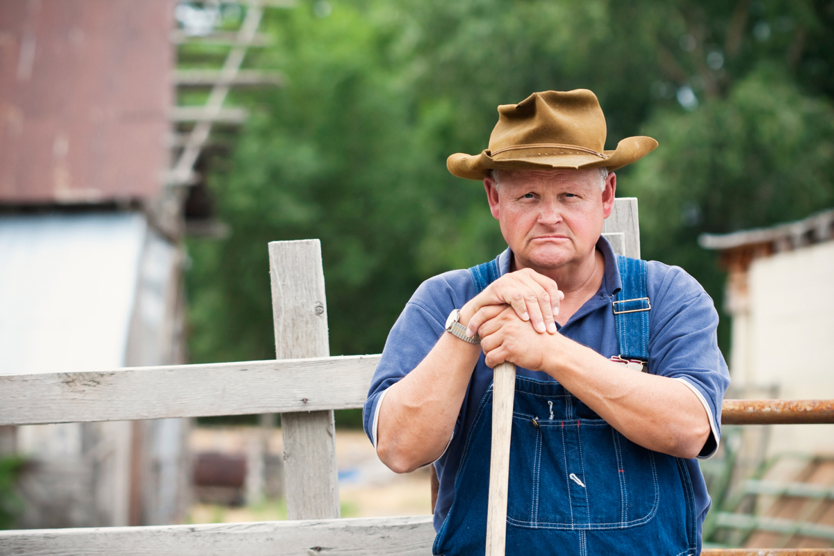 depressed farmer standing outside his barn, looking sad and hoping for smarter policy solutions