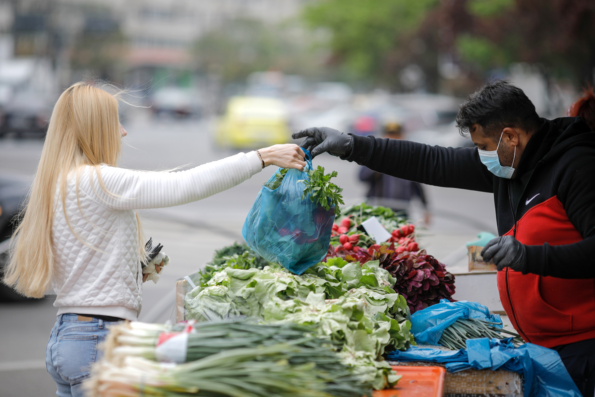 a woman buying food in a plastic bag from a farmers' market