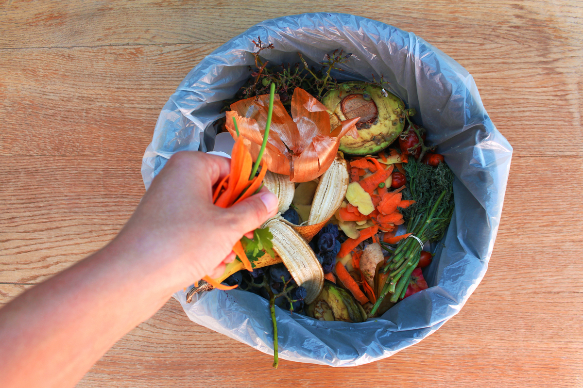 A hand putting food waste into a compost bin.