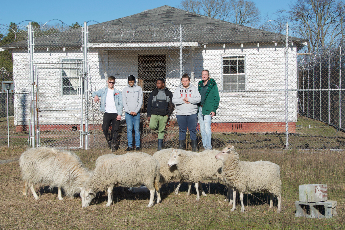 Logan Stern, Robin Patel, Terrence Smith, Michael Adyson Strickland, and Noran Sanford (left to right) stand in the pasture they've created outside the prison yard at the Scotland Correctional Center, which was decommissioned in 2001.