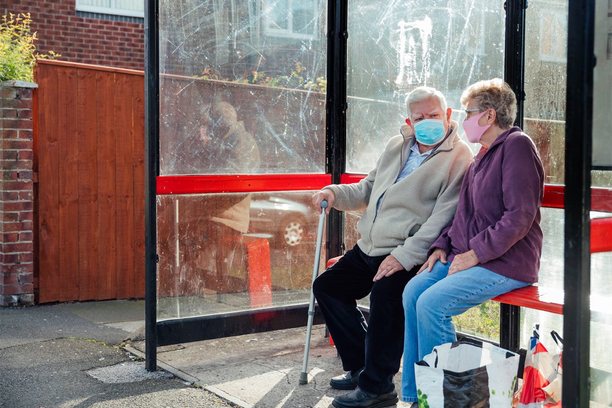 a senior couple waits for public transportation to take them grocery shopping