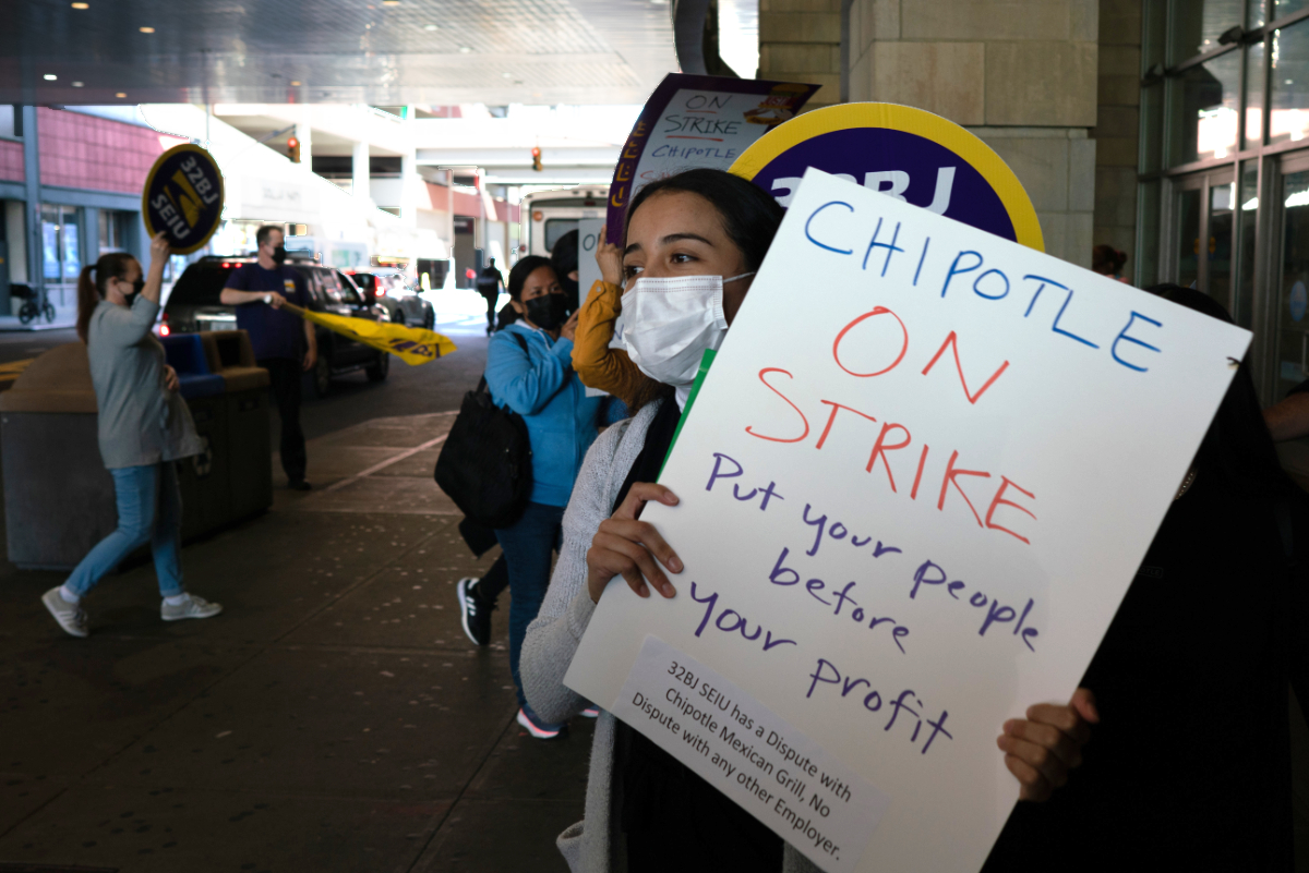 A worker protesting Chipotle holds a sign while marching outside the store. (Photo by Jake Price)