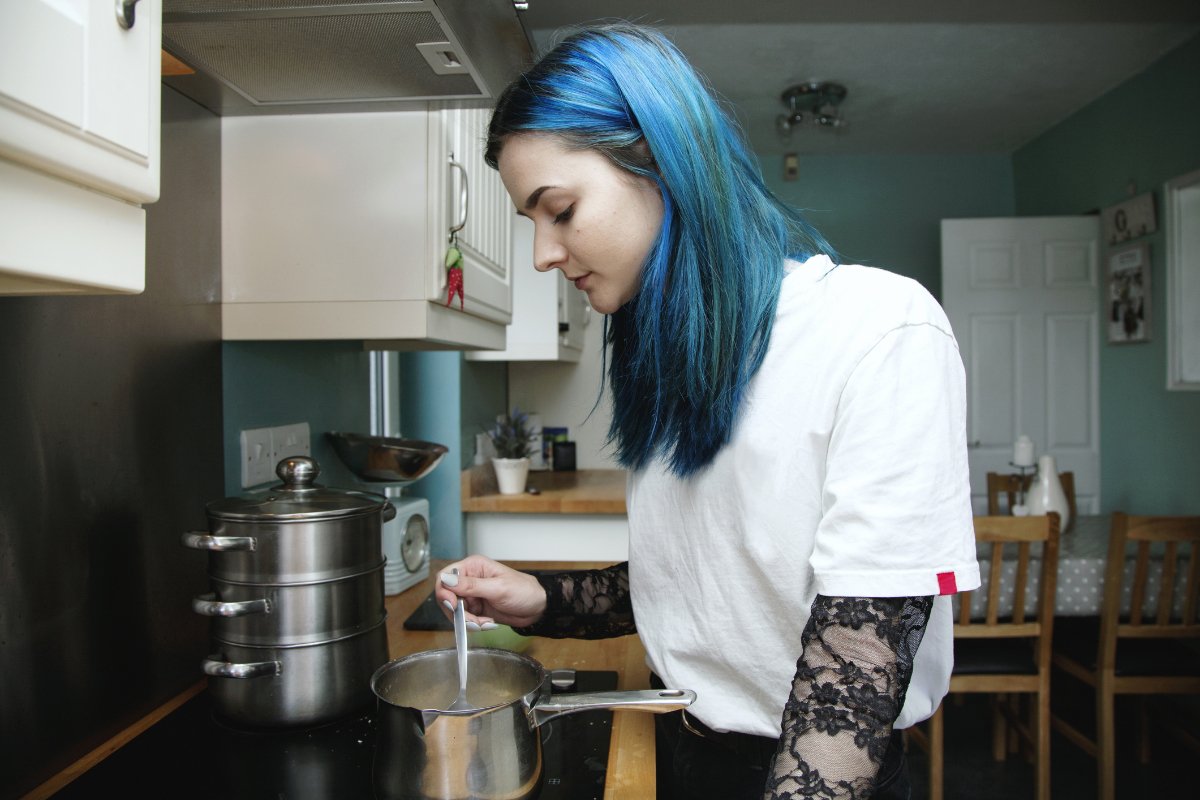 A foster youth teenager with blue hair in the kitchen cooking food