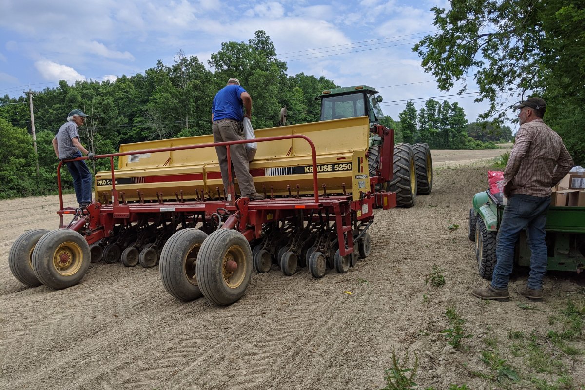 Jean Taber (left), and Carl Taber (center) stand on a grain drill while planting chickpeas for the first time in June 2020.