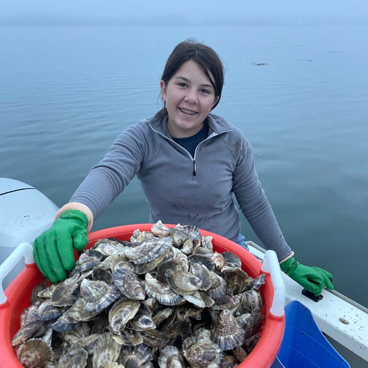 Gaby Zlotkowsky on a boat holding a basket of oysters. (Photo credit: Capshore Photography)